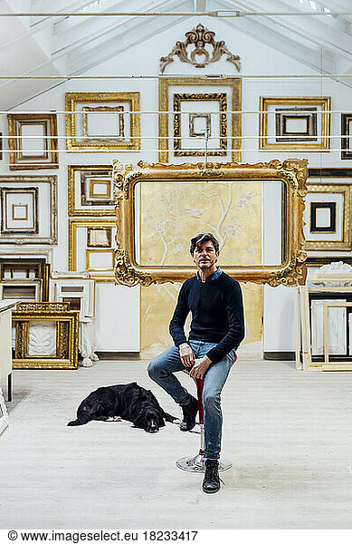 Mature man sitting on chair with dog resting in workshop