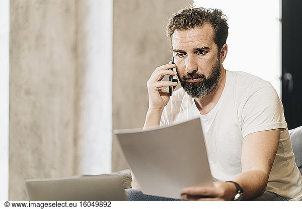 Mature man sitting on couch  talking on the phone  holding papers