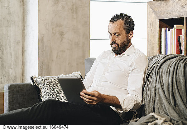 Mature man sitting on couch  using digital tablet