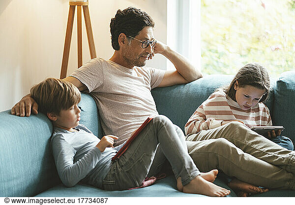 Mature man sitting with daughter and son using tablet PC at home