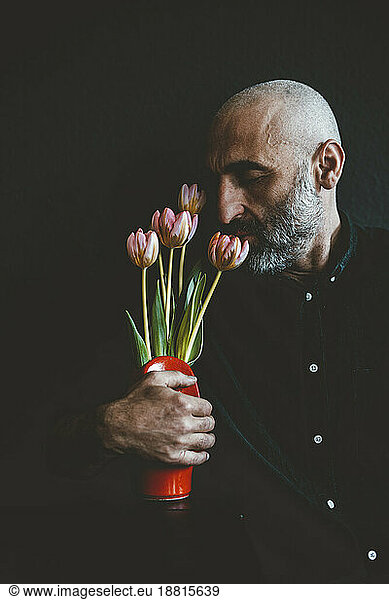 Mature man smelling flowers in vase against black background