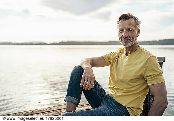 Mature man spending leisure time on jetty by lake