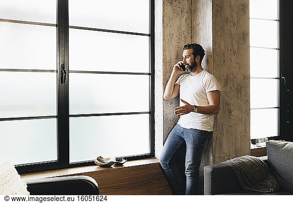 Mature man standing by window  using smartphone