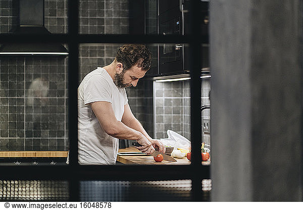 Mature man standing in kitchen  slicing tomatoes