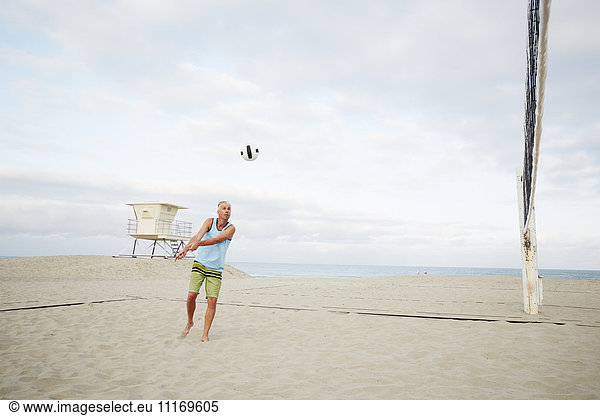 Mature man standing on a beach,  playing beach volleyball.