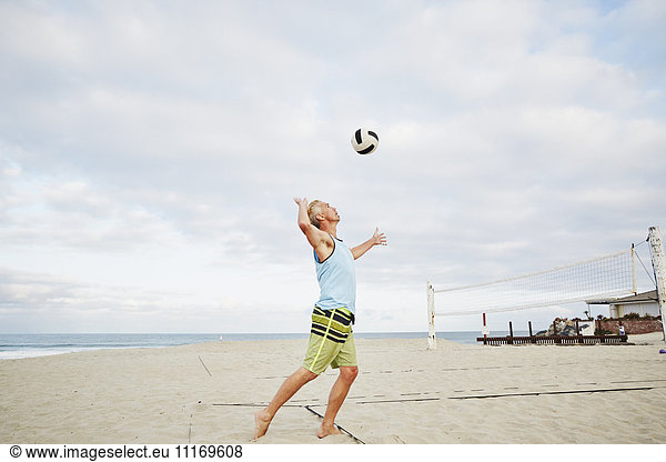 Mature man standing on a beach,  playing beach volleyball.