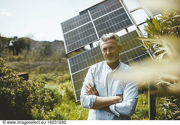 Mature man standing with arms crossed in front of solar panels