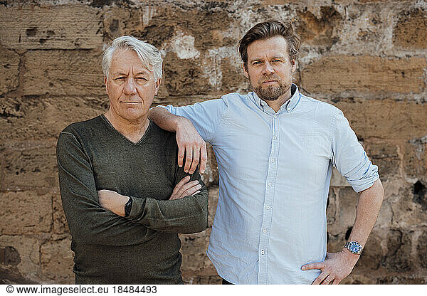 Mature man standing with hand on shoulder of father in front of wall