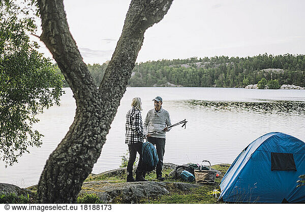 Mature man talking to friend standing by lake during camping