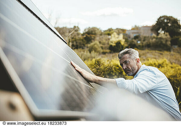 Mature man touching solar panel in garden