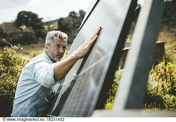 Mature man touching solar panels in garden