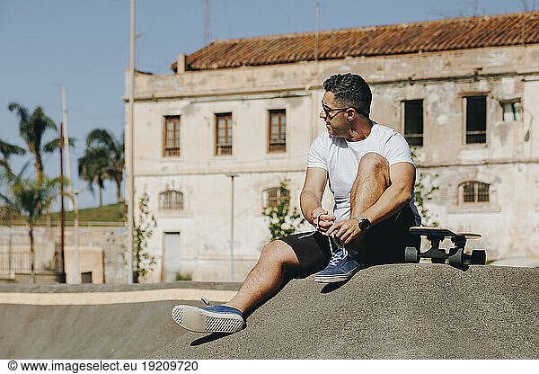 Mature man tying shoelace sitting with skateboard at park