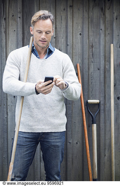 Mature man using smart phone against wooden wall
