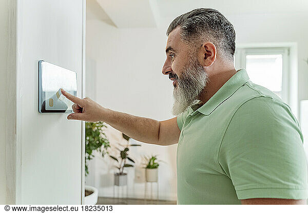 Mature man using tablet PC mounted on wall at home
