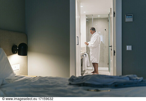 Mature man wearing bathrobe standing in bathroom of hotel room