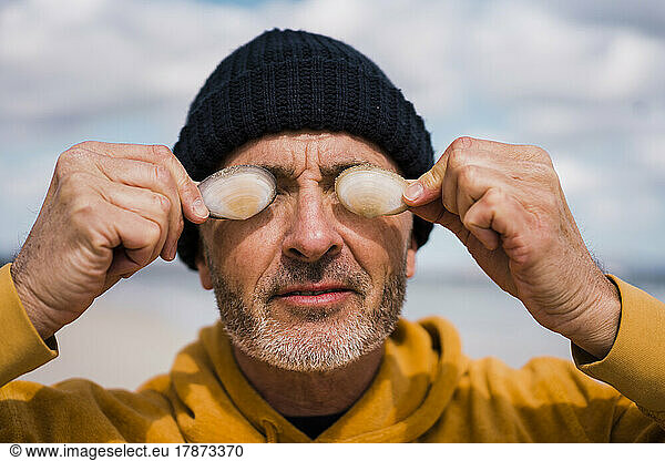 Mature man wearing knit hat covering eyes with seashells