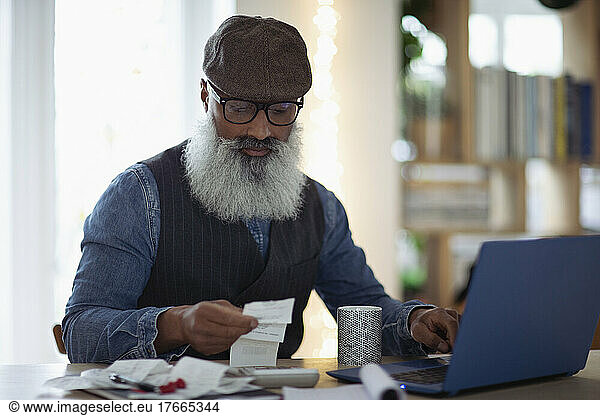 Mature man with beard budgeting at laptop