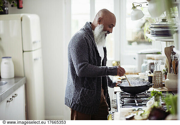 Mature man with beard cooking at kitchen stove