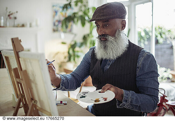 Mature man with beard painting at easel