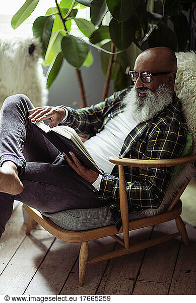 Mature man with beard reading book in armchair