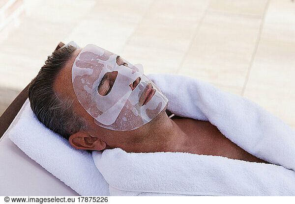 Mature man with facial mask relaxing at pool spa