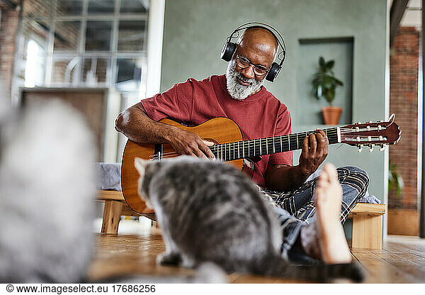 Mature man with headphones playing guitar for cats at home