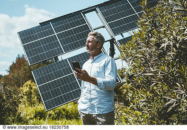 Mature man with mobile phone standing in front of solar panels