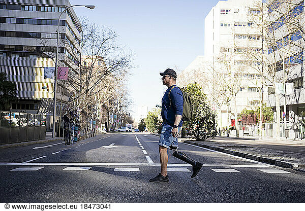 Mature man with prosthetic leg crossing road in city