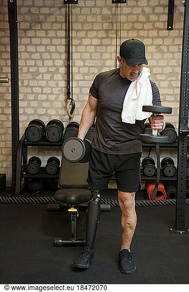 Mature man with prosthetic leg exercising with dumbbell in gym