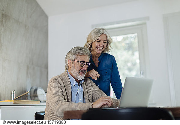 Mature man with wife using laptop on kitchen table at home