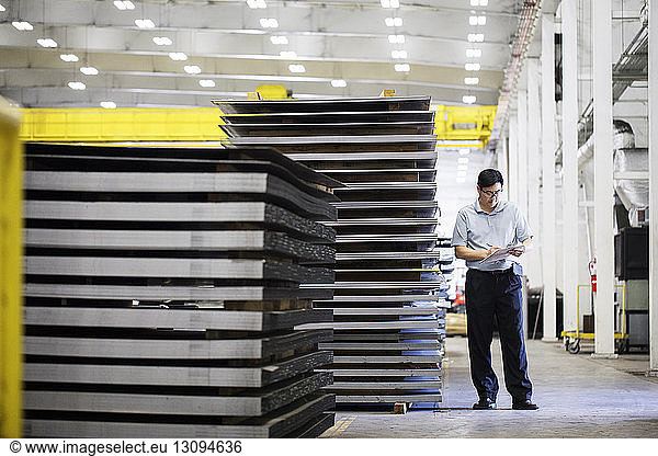 Mature manager examining metal sheets while standing at warehouse