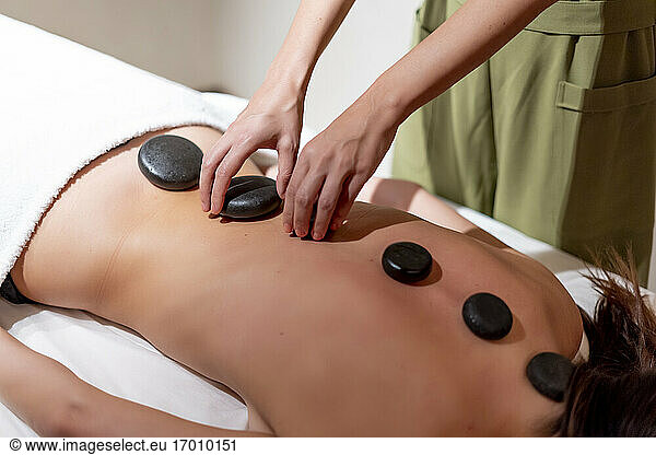 Mature massage therapist positioning stones on female customer's back at health spa