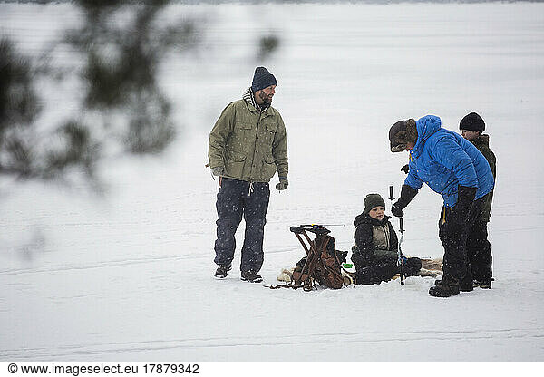 Mature men ice fishing with sons at frozen lake during vacation