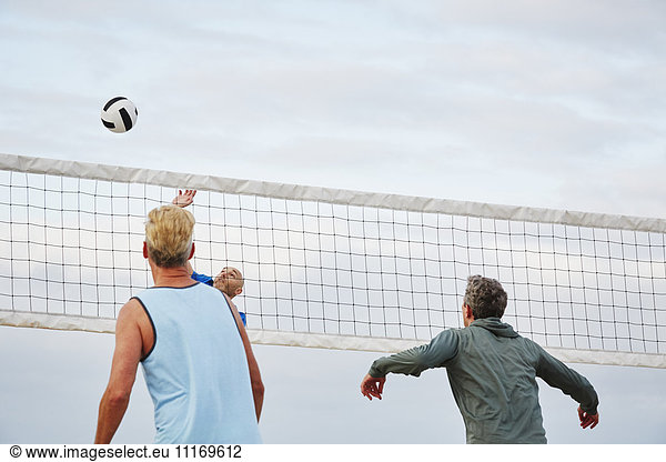 Mature men standing on a beach  playing beach volleyball.