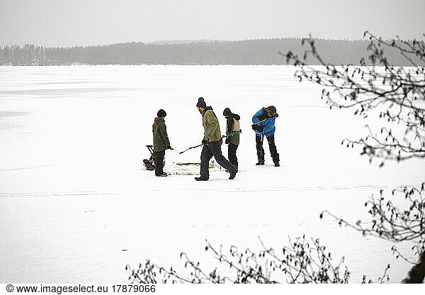 Mature men with sons using ice auger for fishing at frozen lake