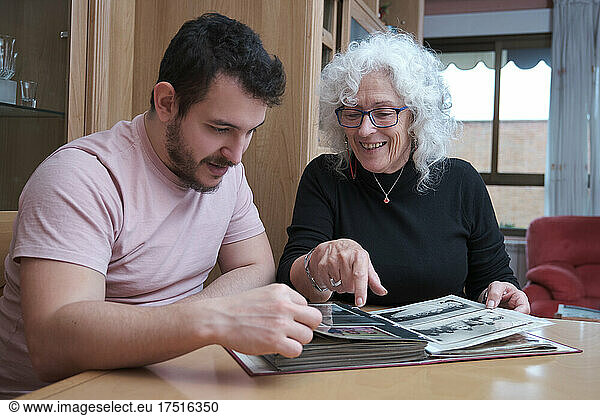 Mature mother and adult son spend time together and look at old album.