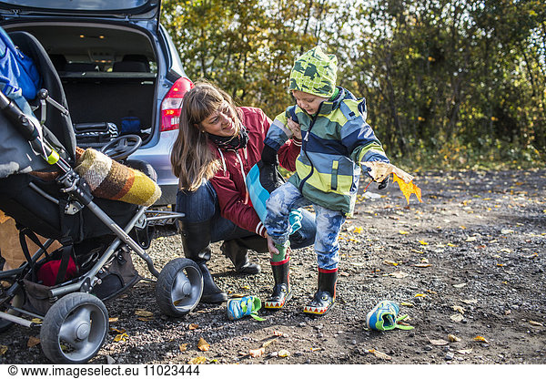 Mature mother assisting boy in wearing rubber boot during picnic