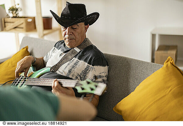Mature musician wearing cowboy hat playing electric guitar at home