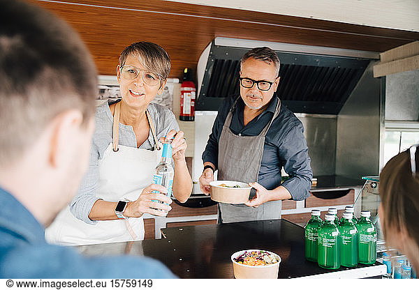 Mature owners serving food and drink to customers while standing in commercial land vehicle