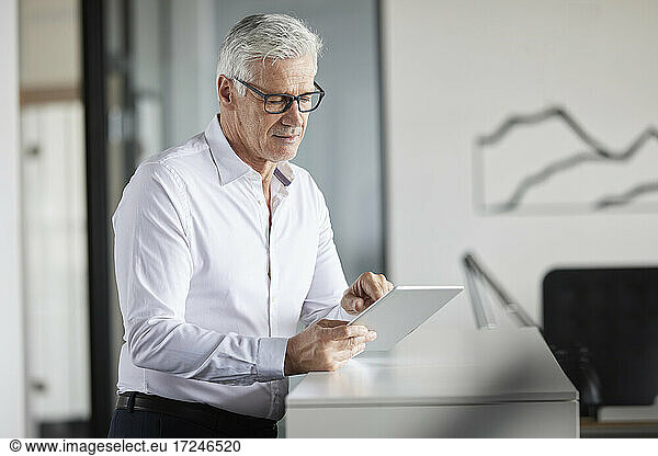 Mature professional using digital tablet while standing in office