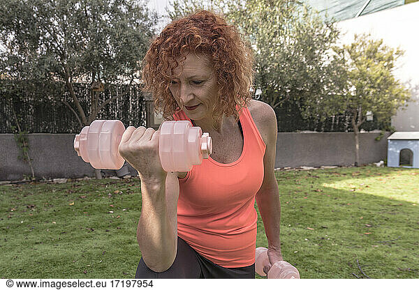 Mature redhead woman lifting dumbbells at garden  home fitness
