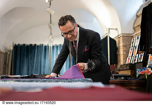 Mature tailor inspecting cloth in studio