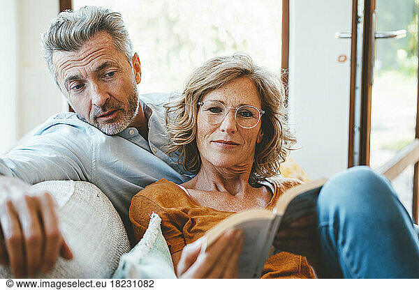 Mature woman and man reading book together at home