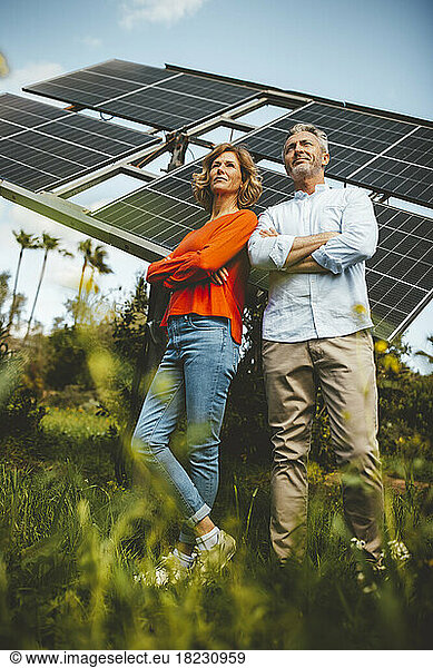 Mature woman and man with arms crossed in front of solar panels