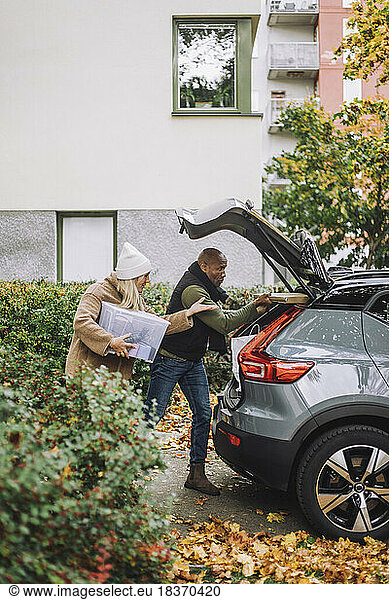 Mature woman assisting man while loading car trunk during relocation of house