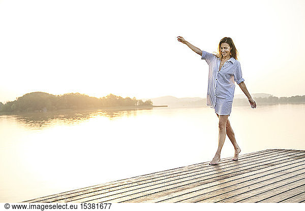 Mature woman balancing on jetty at a lake at sunrise