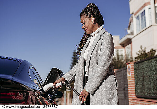 Mature woman charging electric car on sunny day