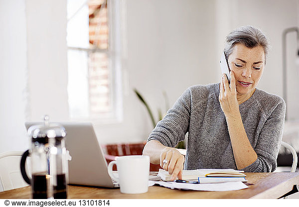 Mature woman communicating on phone while working at table