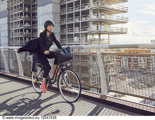 Mature woman cycling on footbridge against building