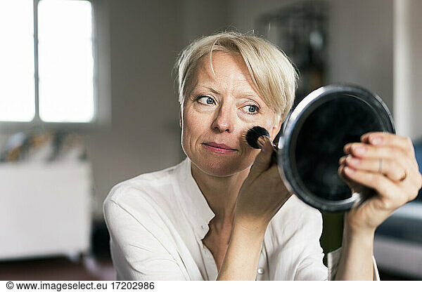 Mature woman doing make-up while looking at mirror